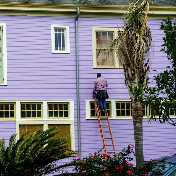 A painter on a ladder working on the weatherboards of a two-storey house